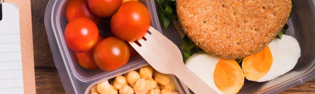 gezonde-lunch 1600×480 Gesunde Mahlzeit: Tomaten, Kichererbsen, Ei und Vollkornbrot im Bento-Behälter.