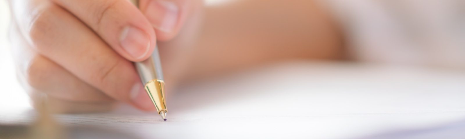 Hand mit Stift schreibt auf einem Dokument, im Hintergrund ein helles, natürliches Licht.