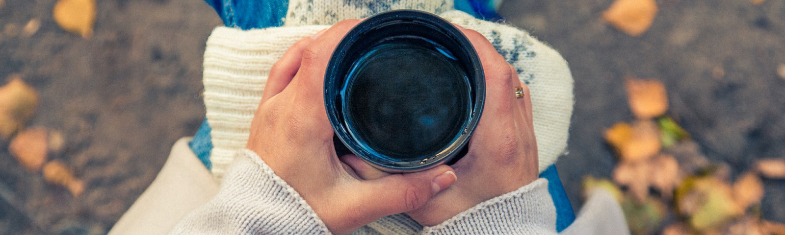 Zelf thee maken Hände halten eine Thermoskanne mit heißem Getränk, umgeben von Herbstlaub, ideal für Fitness-Ernährung.