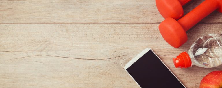 Fitness-Outfit: Hanteln, Wasserflasche, Handy und Apfel auf Holztisch.