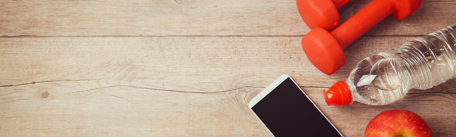 Fitness-Outfit: Hanteln, Wasserflasche, Handy und Apfel auf Holztisch.