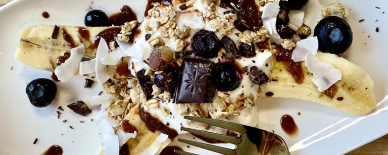 Fitness-Dessert: Banane mit Joghurt, Granola, Beeren, Kokoschips und Schokolade.