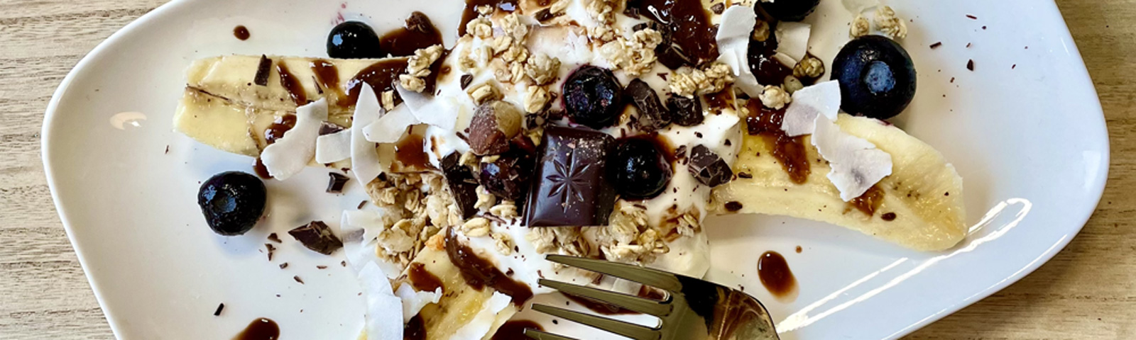 recept-bananensplit Fitness-Dessert: Banane mit Joghurt, Granola, Beeren, Kokoschips und Schokolade.