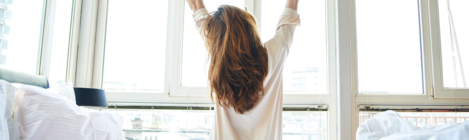 Frau streckt sich im Bett vor einem hellen Fenster, bereit für einen energiegeladenen Tag – perfekt für Fitness- und Ernährungsprogramme.
