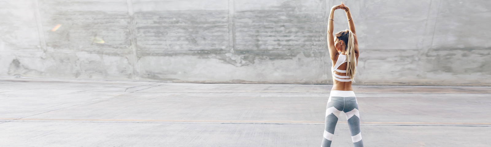 Sportlerin in weißem Sport-BH und grau-weißer Leggings streckt Arme über dem Kopf, Fitness und gesunde Ernährung.