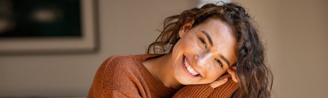 Lächelnde Frau mit Sommersprossen in orangefarbenem Pullover – Fitness und gesunde Ernährung.