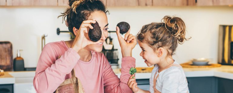 Mutter und Kind spielen mit Avocados in der Küche und lernen gesunde Ernährung.