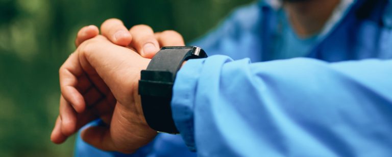 Person prüft Smartwatch mit blauem Trainingsanzug, Fokus auf Fitness.