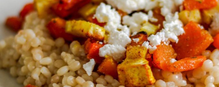 Pearl couscous salad with roasted vegetables, cherry tomatoes and fresh herbs in a bowl, drizzled with lemon-olive oil dressing.