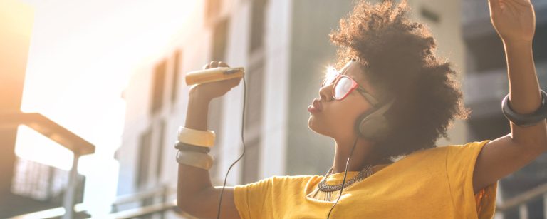 Person relaxing with headphones in a cozy room at dusk, soft warm lighting and a calm playlist on a phone screen.