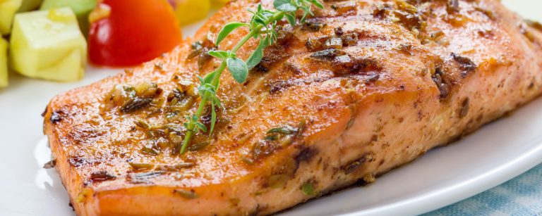 Grilled salmon fillets topped with fresh mango–avocado salsa on a plate, with lime wedges and herbs.