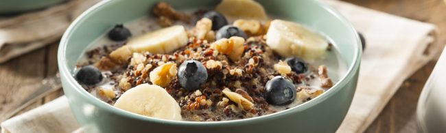 Colorful quinoa breakfast bowl topped with yogurt, fresh berries, nuts and seeds on a bright morning table.