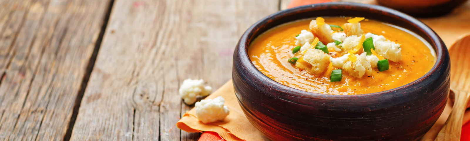 A steaming bowl of creamy sweet potato and cauliflower soup, garnished with fresh parsley, placed on a wooden table.