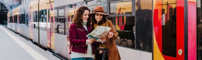 Zwei Frauen studieren mit einem Stadtplan eine Zugroute, ideal für Fitness-Reiseplanung.
