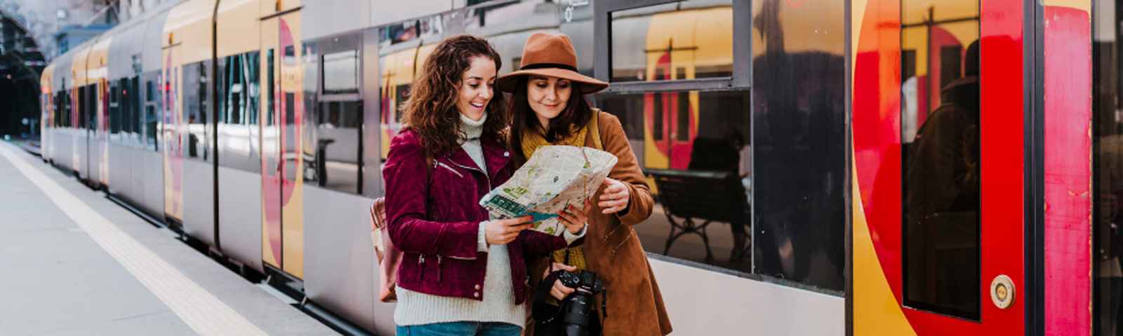 Zwei Frauen studieren mit einem Stadtplan eine Zugroute, ideal für Fitness-Reiseplanung.