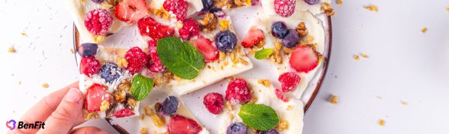 Frozen yogurt bites topped with strawberries, blueberries and granola on a parchment-lined tray