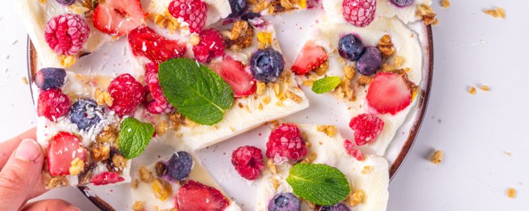 Frozen yogurt bites topped with strawberries, blueberries and granola on a parchment-lined tray